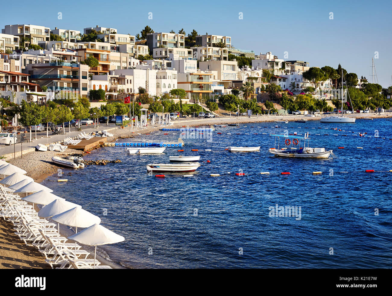 Hotels and White Umbrellas near lagoon with boats on the beach in Bodrum, Turkey Stock Photo