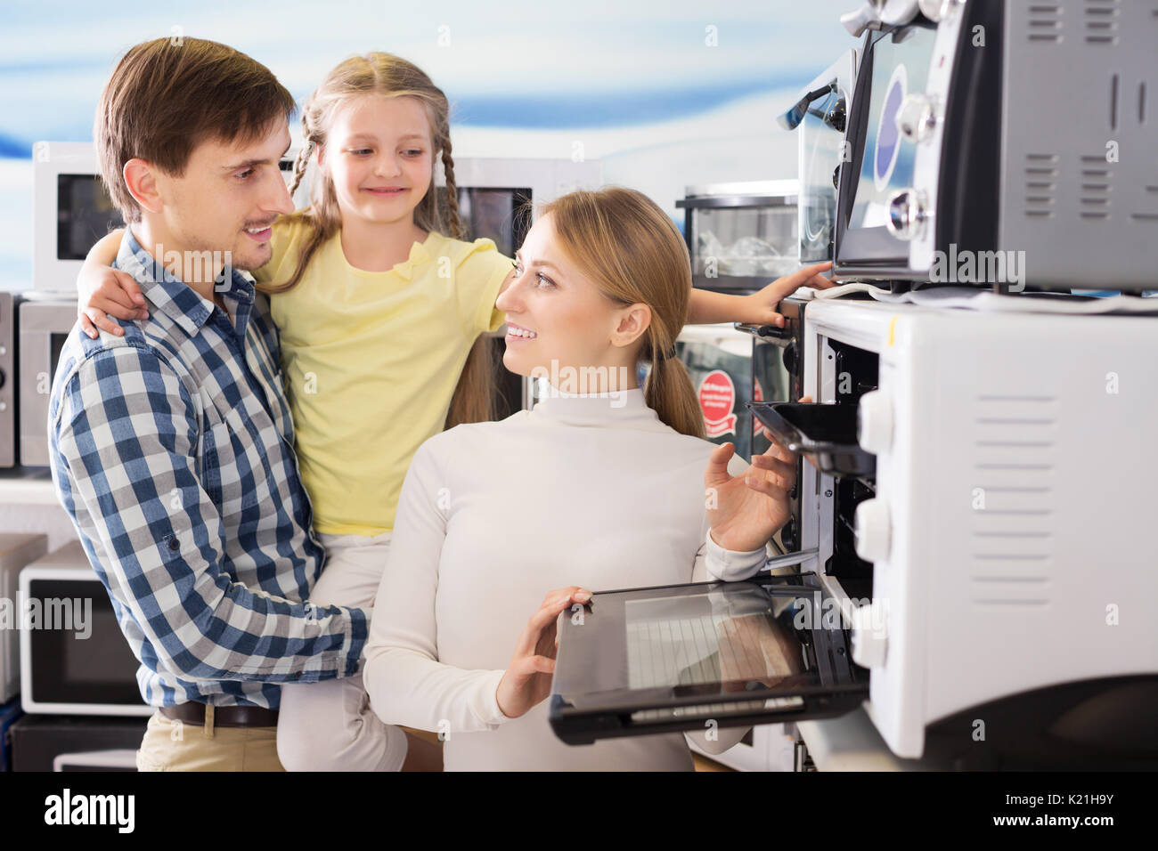 Cheerful man and woman with girl buying modern microwave in store with electronics Stock Photo