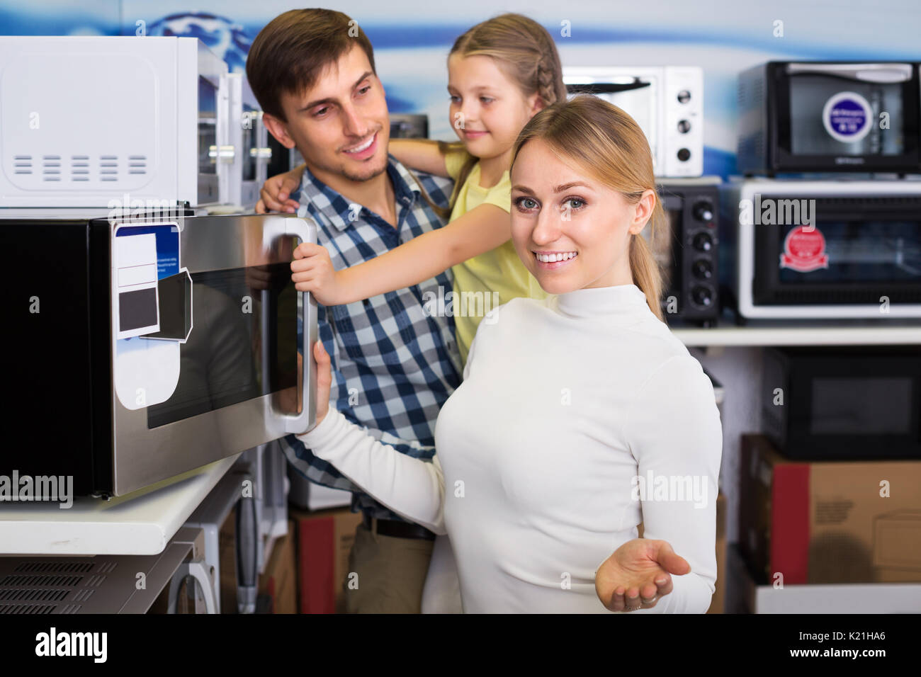 Happy man and woman with girl buying modern microwave in store with electronics Stock Photo