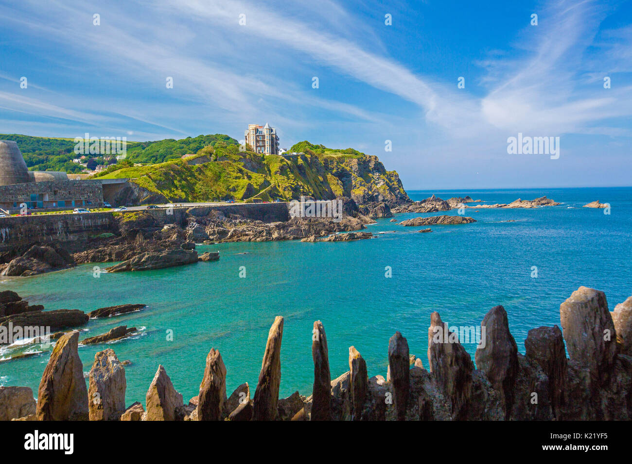 Sprawling town hemmed by sheltered beach, and blue waters of ocean lapping at rocky coastline under blue sky at Ilfracombe, North Devon, England Stock Photo