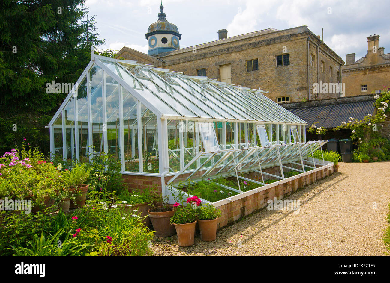 Greenhouse with potted plants and brightly coloured flowers beside it at Rousham gardens, Oxfordshire, England Stock Photo