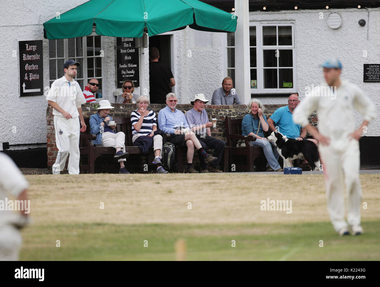 Spectators sat outside the Barley Mow pub watching a village cricket match between Tilford and Grayswood being played on the green in Tilford, Surrey, on Saturday July 15, 2017. Stock Photo