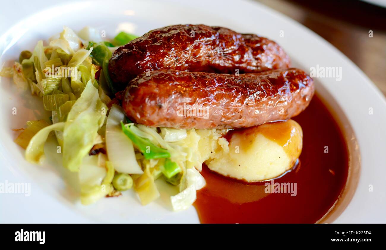 Sausage and mashed potato with seasonal greens served with red wine gravy on a white plate Stock Photo