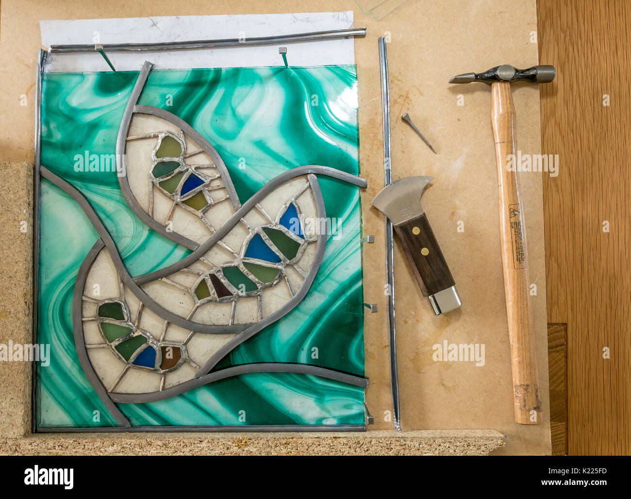 Work in progress making stained glass and sea glass art work project with lead came. Work board with lead came, hammer, horseshoe nails and lead knife Stock Photo