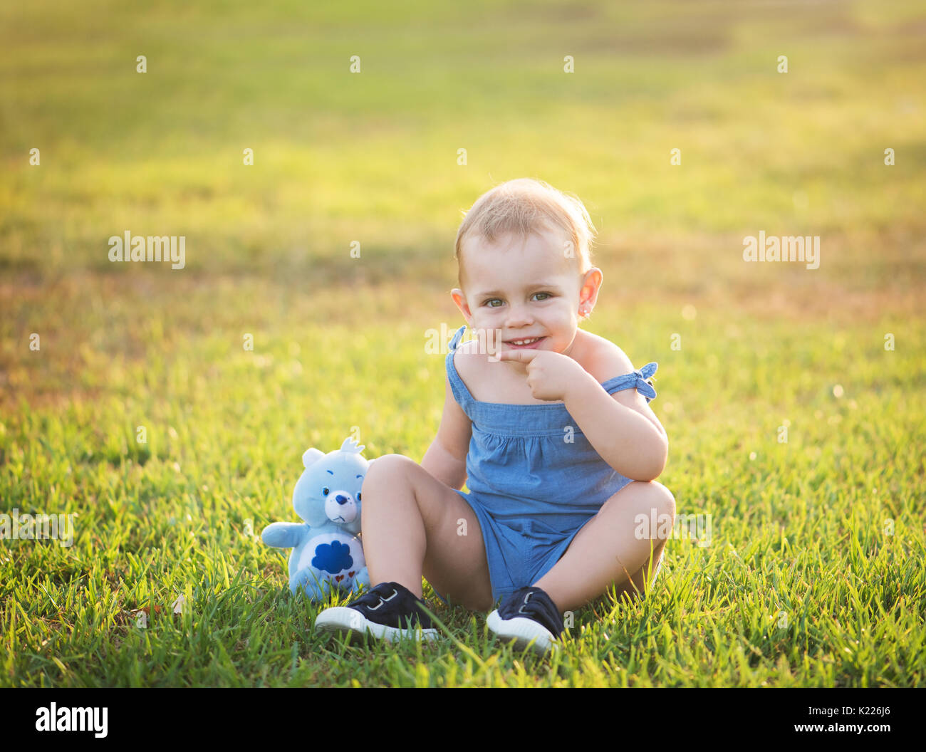 cute little girl is sitting on the grass in a park with a stuffed toy ...