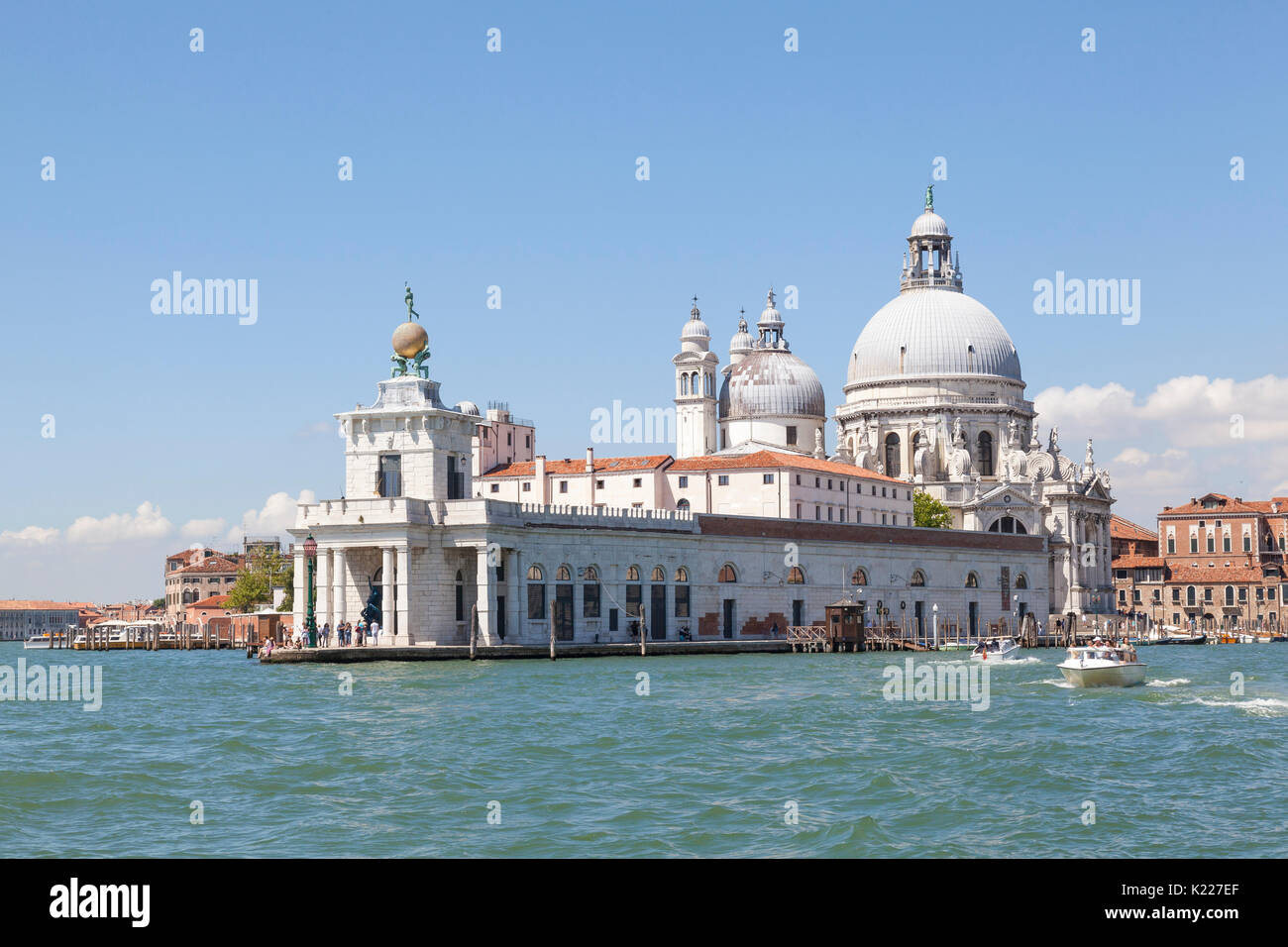 View from the lagoon of Punta della Dogana and Basilica Santa Maria della Salute, Venice, Italy on a sunny day with tourists and water taxis. This use Stock Photo