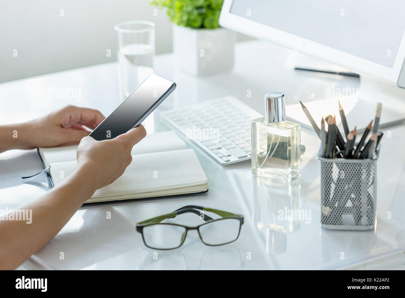 Close-up of female hands using smart phone while working on computer at ...