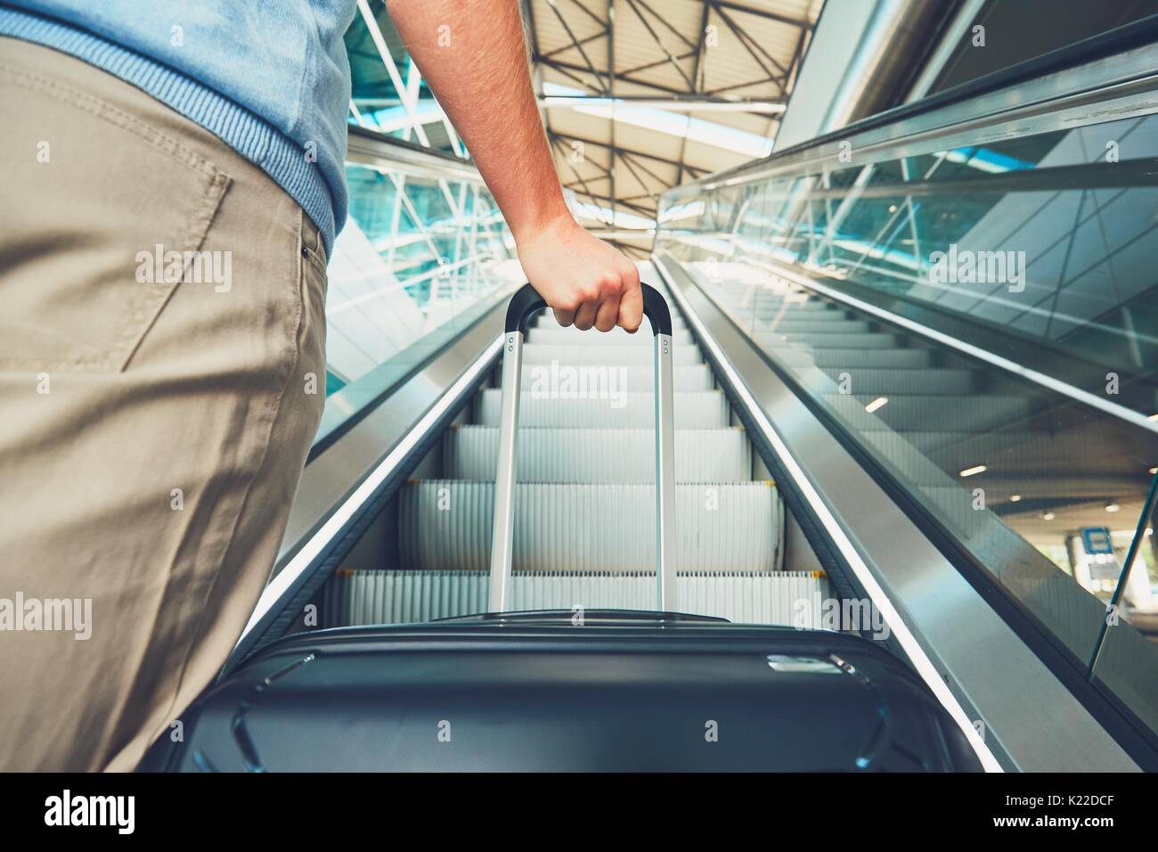 Man traveling by airplane. Hand of the passenger with luggage on the escalator at the airport. Stock Photo