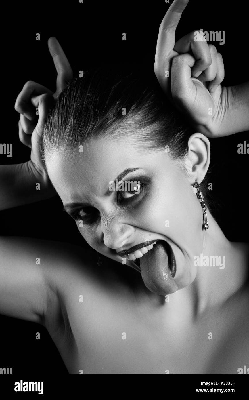fun luxury woman show horns and tongue on black background, looking at camera, monochrome Stock Photo