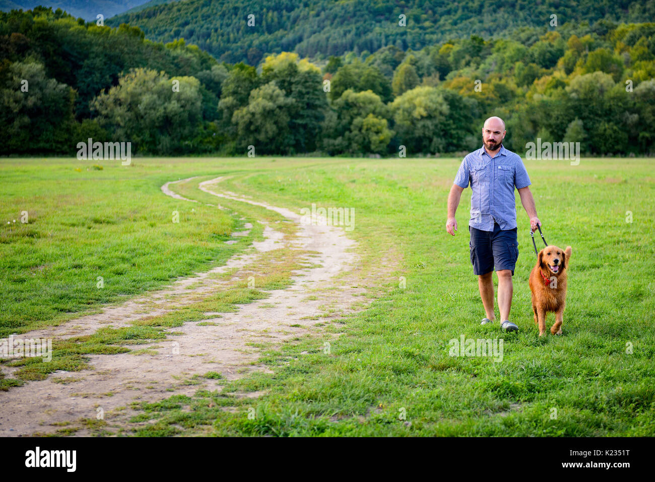 Young handsome Hipster man taking his family pet dog golden retriever for a walk in a park. Stock Photo