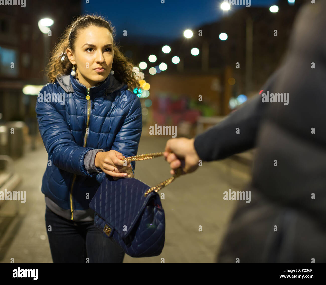 Frightened young woman and robber trying to steal bag at night Stock Photo