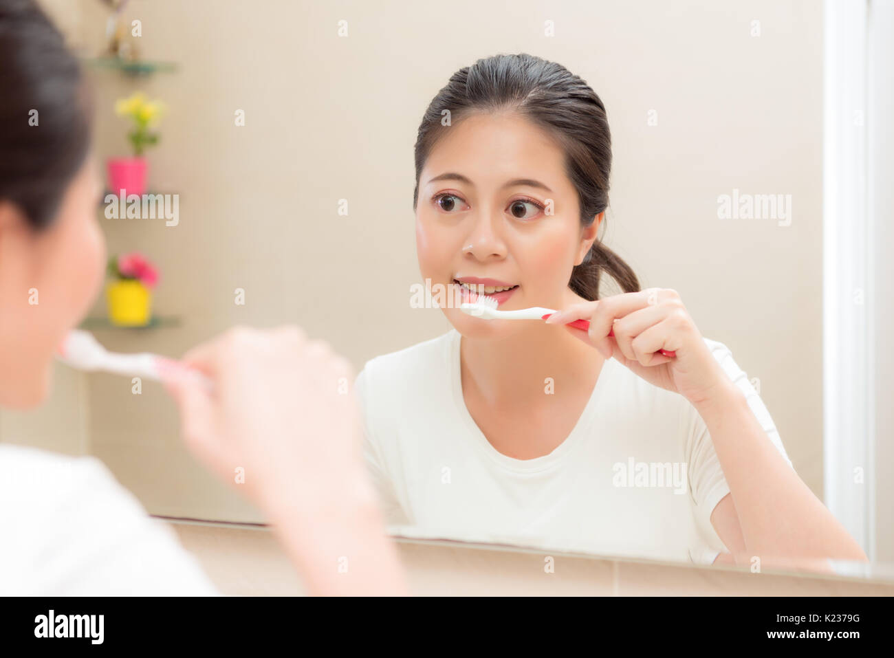 young smiling housewife using toothbrush cleaning teeth after eating food or waking up in morning standing on bathroom looking mirror brushing. Stock Photo