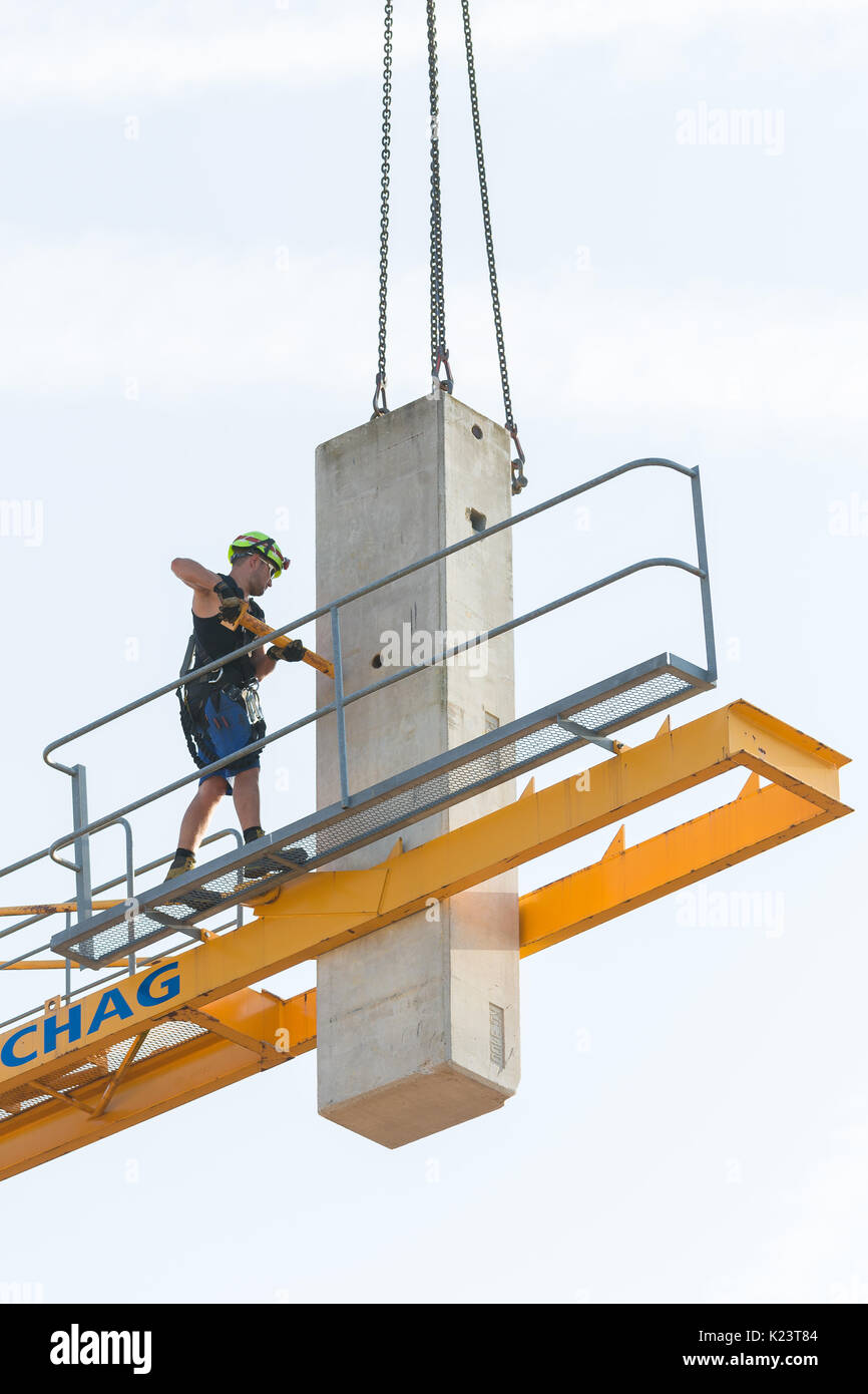 Worker in the process of removing a tower crane disassembling it bit by bit. The ballast support bar is removed from the concrete counterweight during the removal. Stock Photo