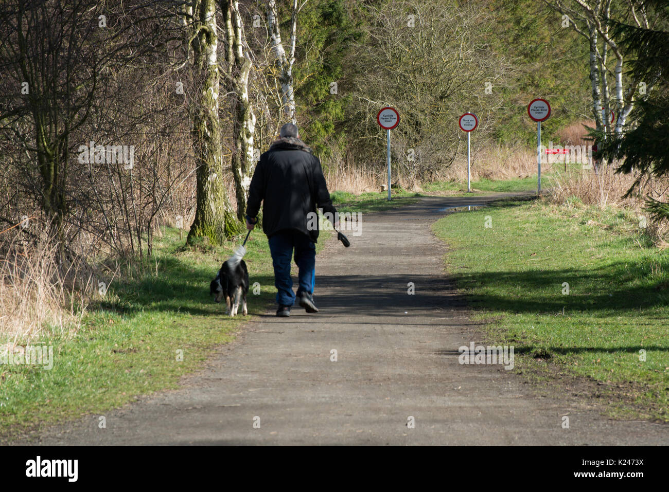 Single dog walker carrying excrement bag to provided container and with local authority safety notices on country side path Stock Photo