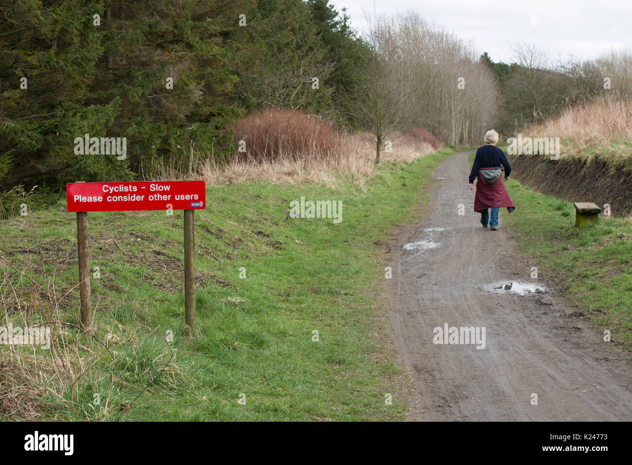 Public path in countryside showing lone walker and notice with request to cyclists to consider other path users Stock Photo