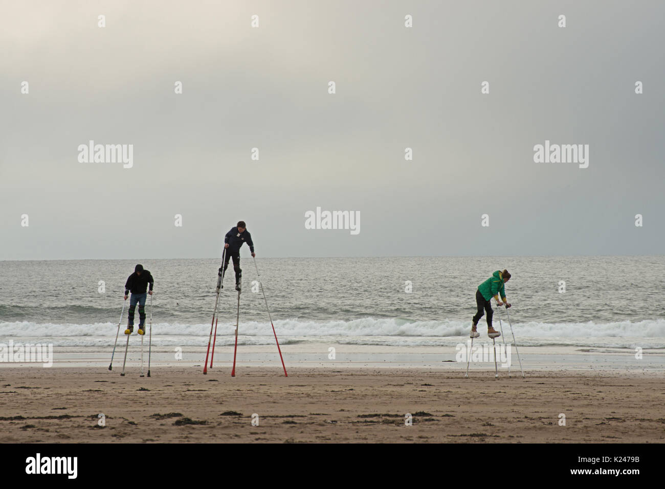 Three stilt walkers in practice along the Northumberland coast with the sea in the background as rain approaches Stock Photo