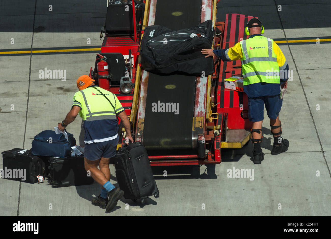 Luggage being unloaded by baggage handlers from passenger airplane at Sydney International Airport, New South Wales, Australia. Stock Photo