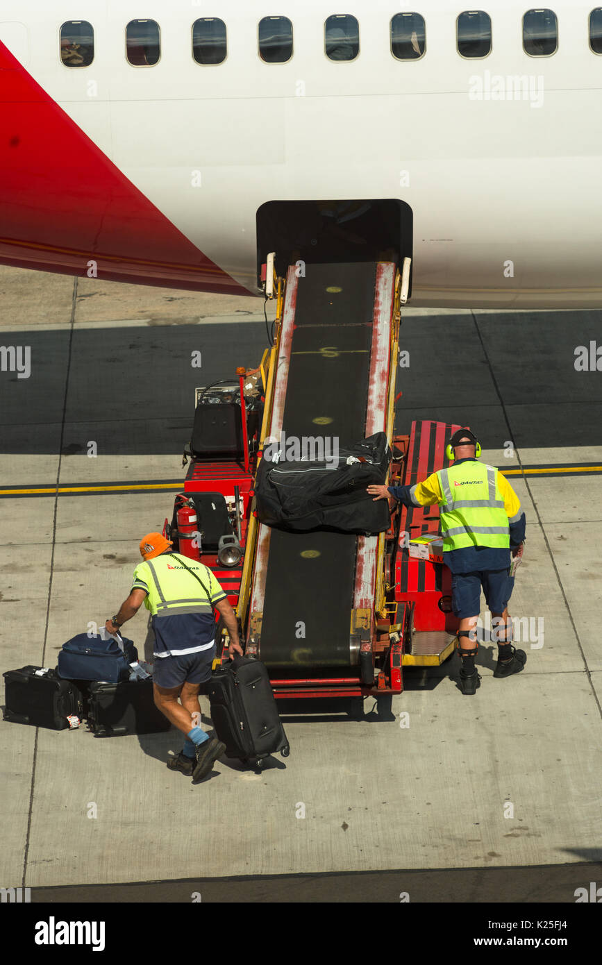 Luggage being unloaded by baggage handlers from passenger airplane at Sydney International Airport, New South Wales, Australia. Stock Photo