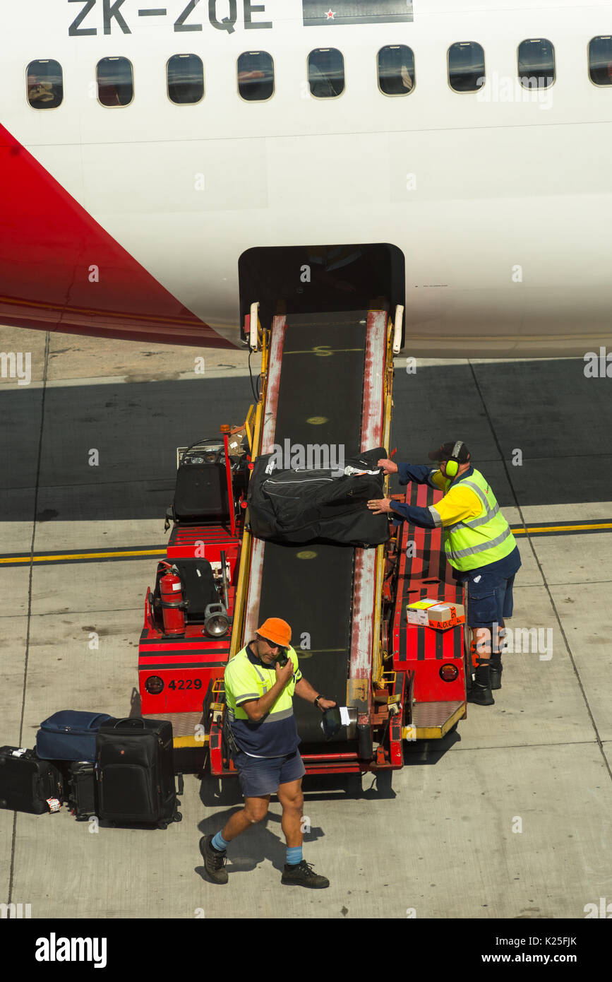 Luggage being unloaded by baggage handlers from passenger airplane at Sydney International Airport, New South Wales, Australia. Stock Photo