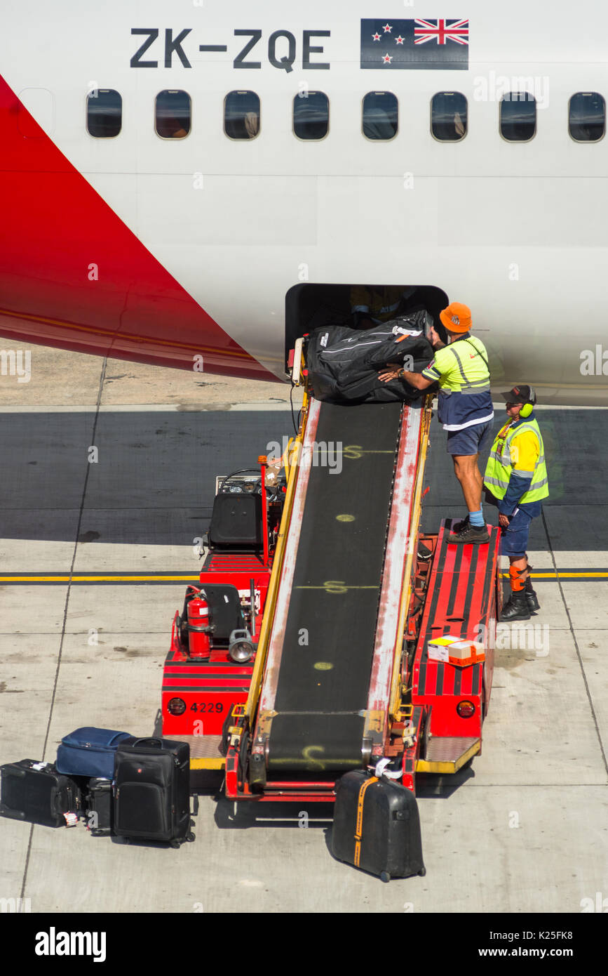 Luggage being unloaded by baggage handlers from passenger airplane at Sydney International Airport, New South Wales, Australia. Stock Photo