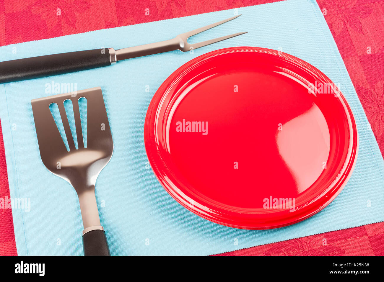 A set of barbecue tools and plastic plate on a blue cloth mat symbolizing barbecue time. Stock Photo