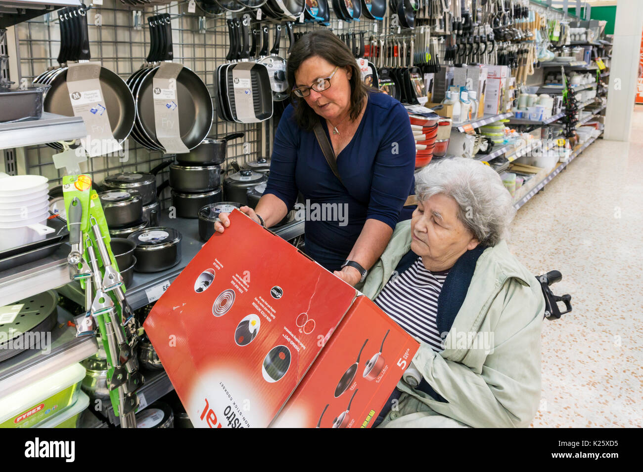 Carer or assistant helping an elderly woman in a wheelchair choose some new saucepans in a supermarket. Stock Photo