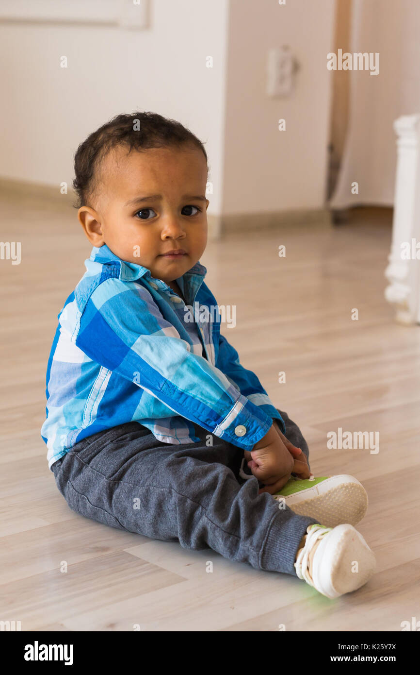 Small child tries to put on his shoes. Mixed race baby boy with