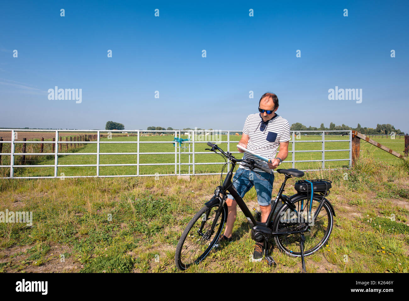 A middle-aged man with an e-bike stands along the side of the road and looks at a road map Stock Photo