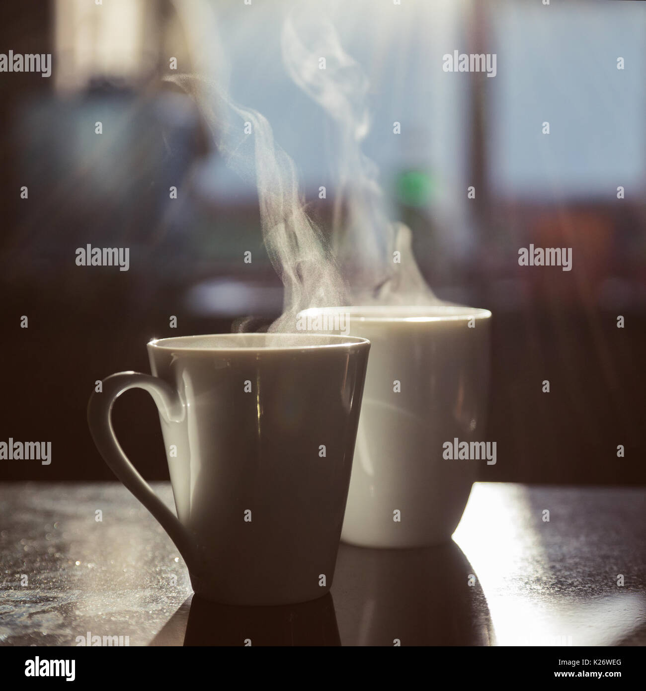 Two cups of coffee, steaming, standing on table, backlit Stock Photo