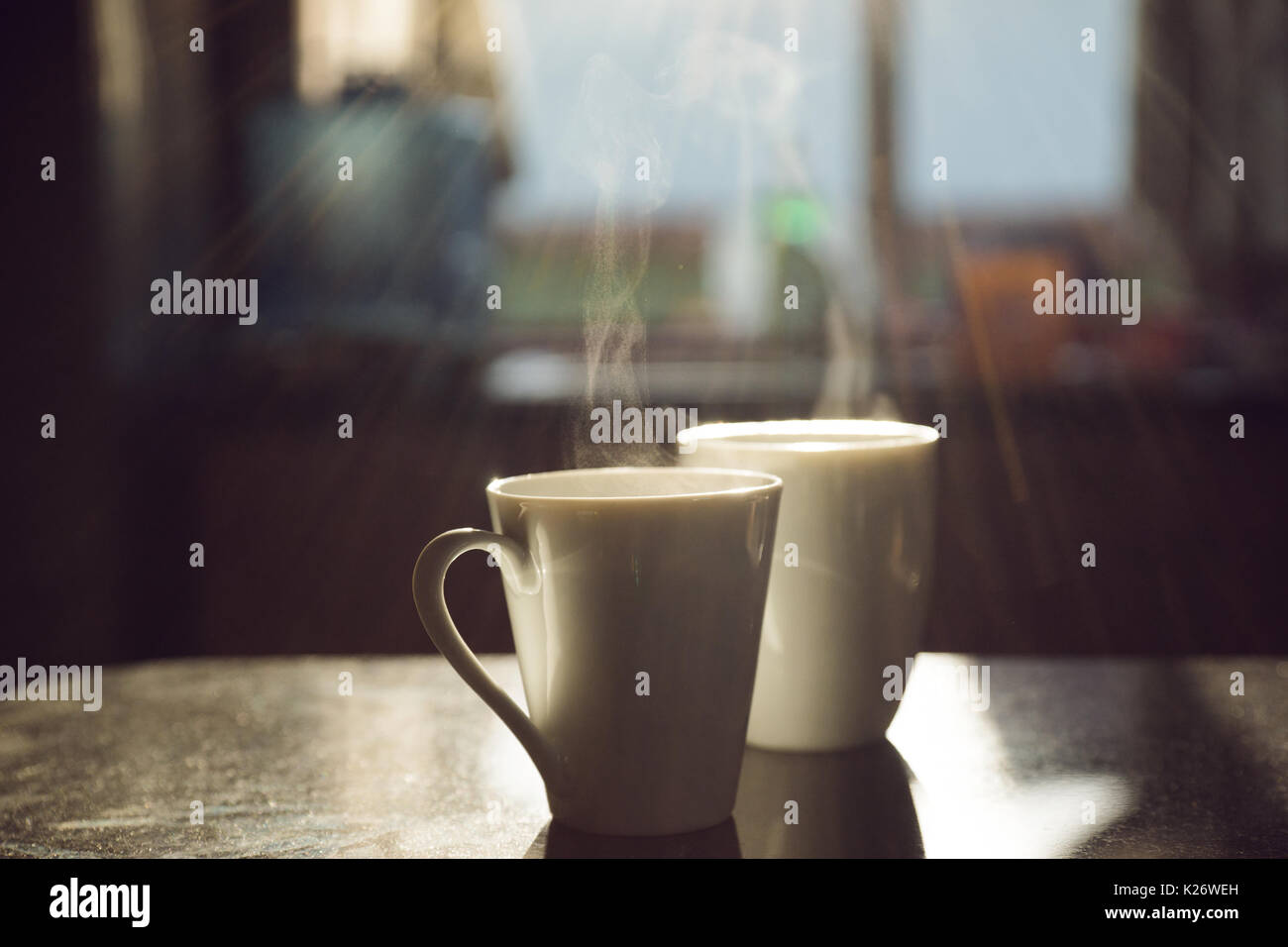 Two cups of coffee, steaming, standing on table, backlit Stock Photo