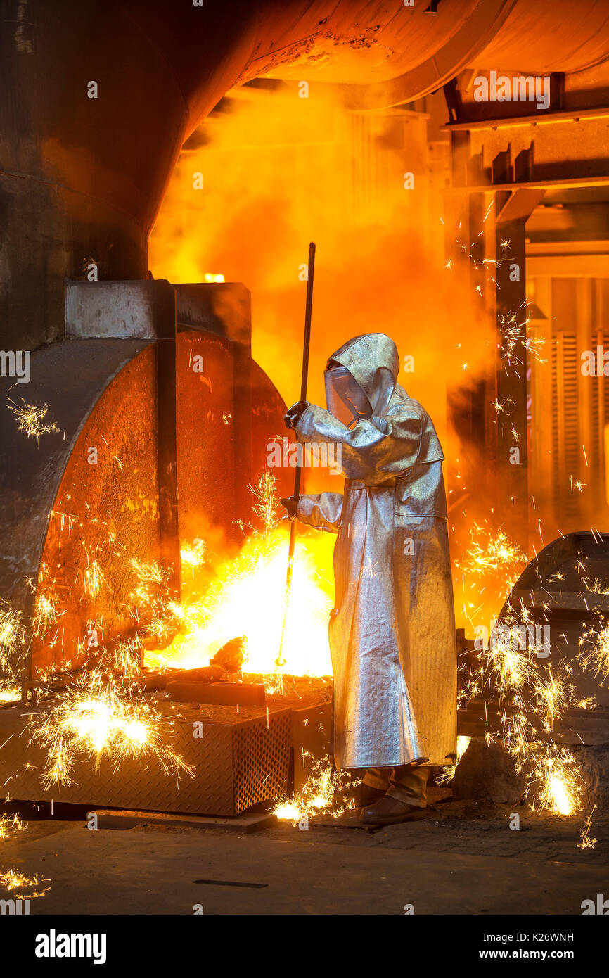 A steel worker in a protective suit taking a 1500 ° hot raw iron sample