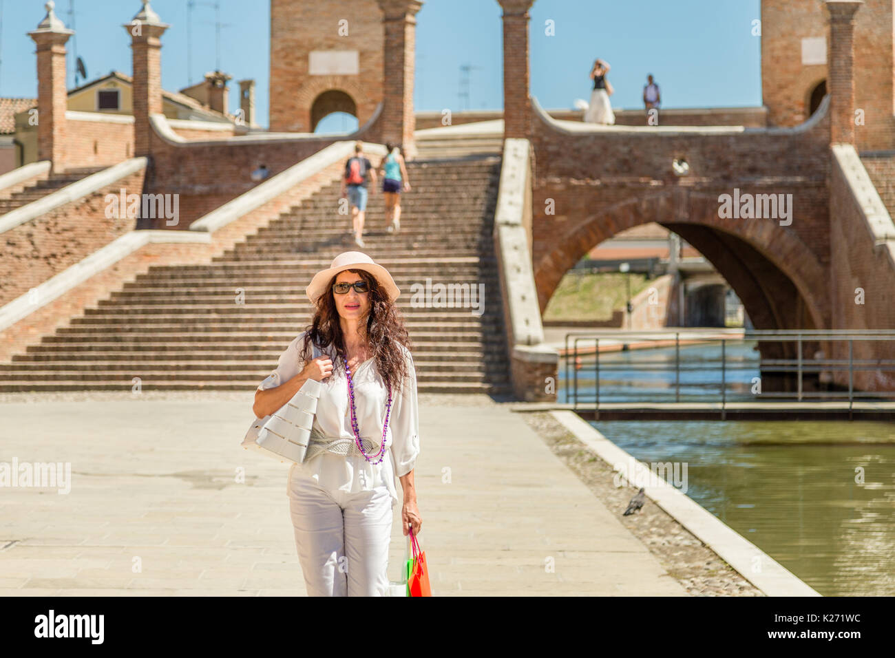 classy mature woman with wide hat and sunglasses near walking along channel in lagoon town  in Italy Stock Photo