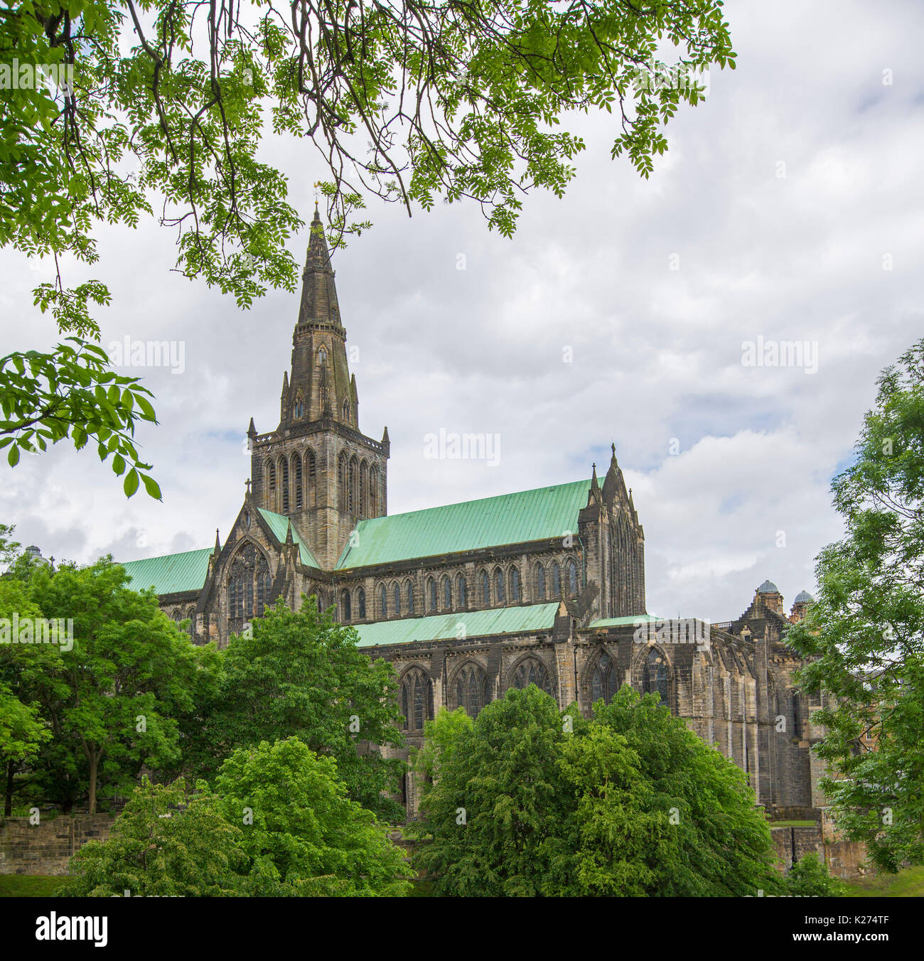 Historic Glasgow cathedral with light green roof and framed by foliage of trees, viewed from nearby Necropolis, in Scotland Stock Photo