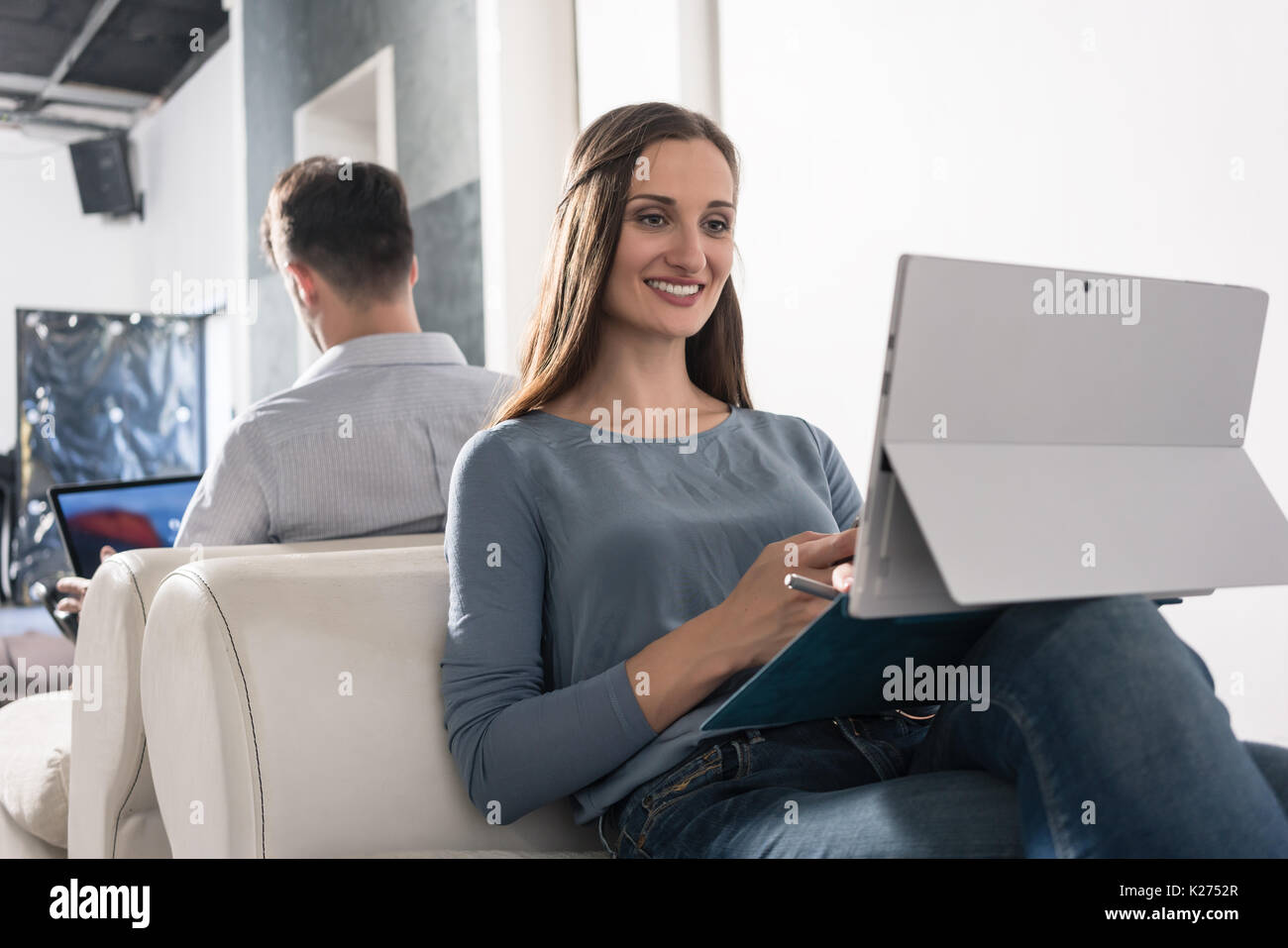 Woman sitting in armchair with smartphone and laptop PC Stock Photo