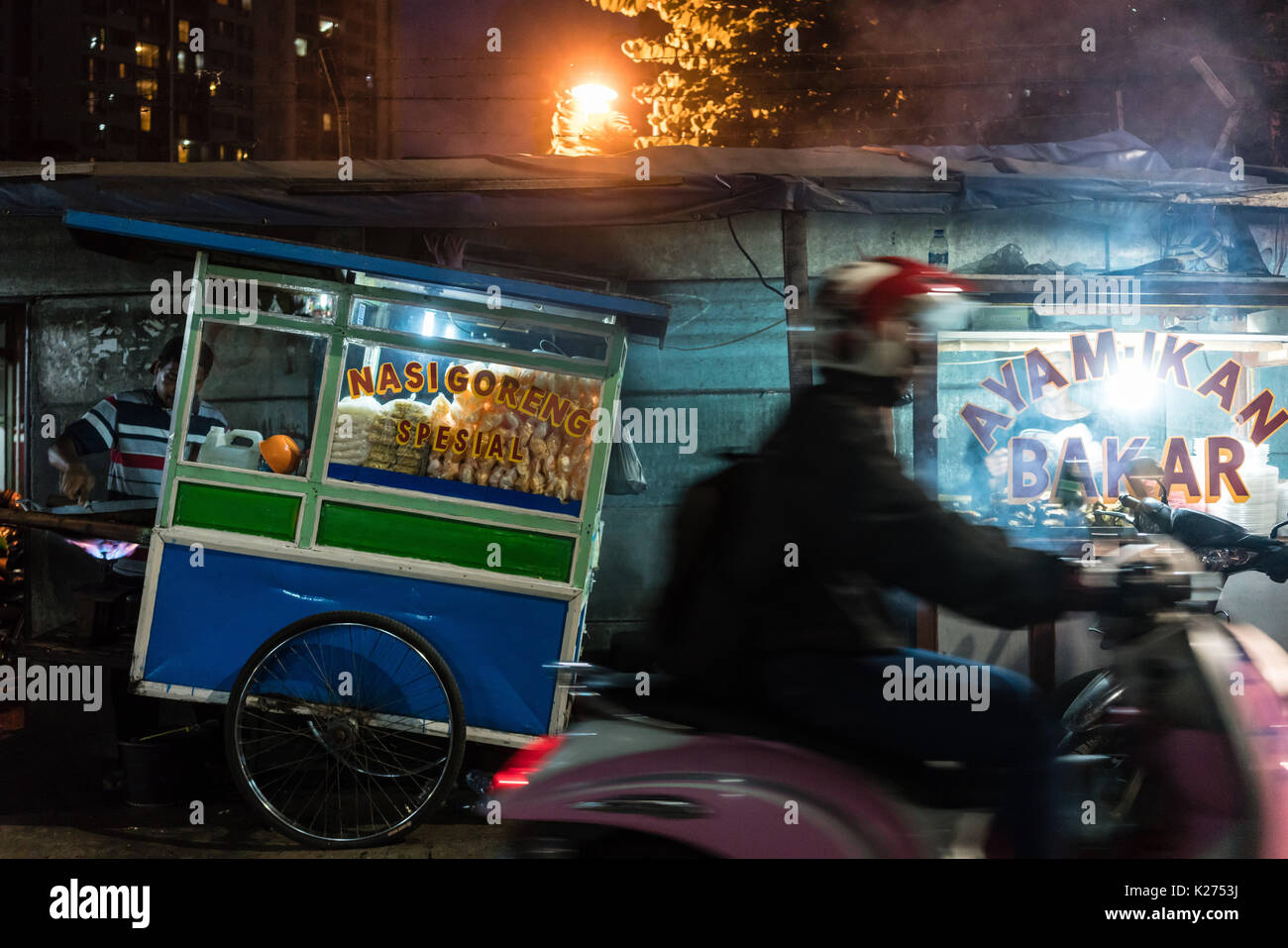 Man riding a scooter on a street with food stalls in a poor dist Stock Photo