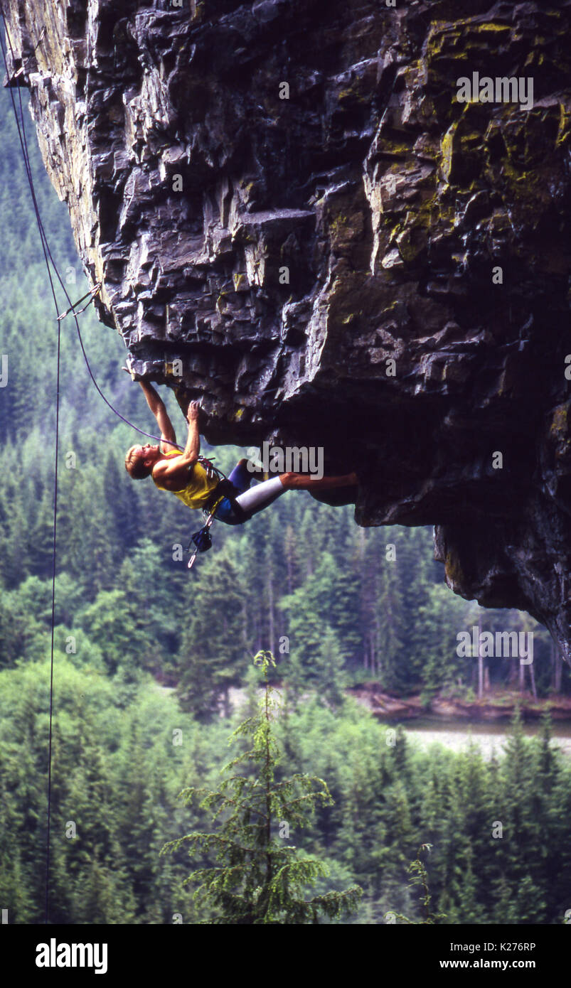 A man rock climbing on top rope on a severely overhanging rock climbing route with a forested mountainside in the background. Stock Photo
