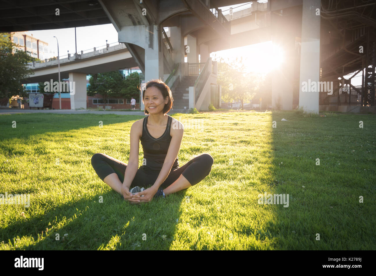 A woman stretches on the grass of a city park. Stock Photo