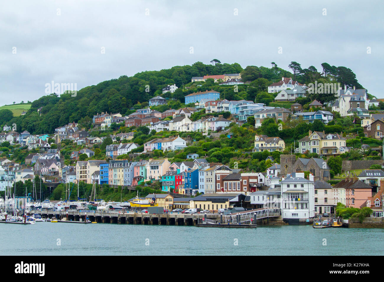 Coastal town of Dartmouth with colourful houses crammed on tree-cloaked hillside rising above harbour and ferry terminal in Devon, England Stock Photo