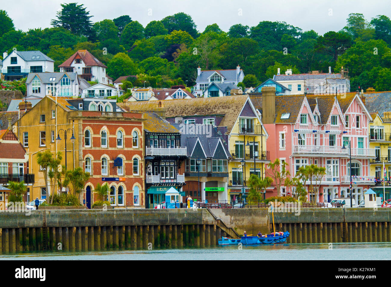 Coastal town of Dartmouth with brightly coloured buildings at foot of tree-cloaked hillside beside harbour and wharf in Devon, England Stock Photo