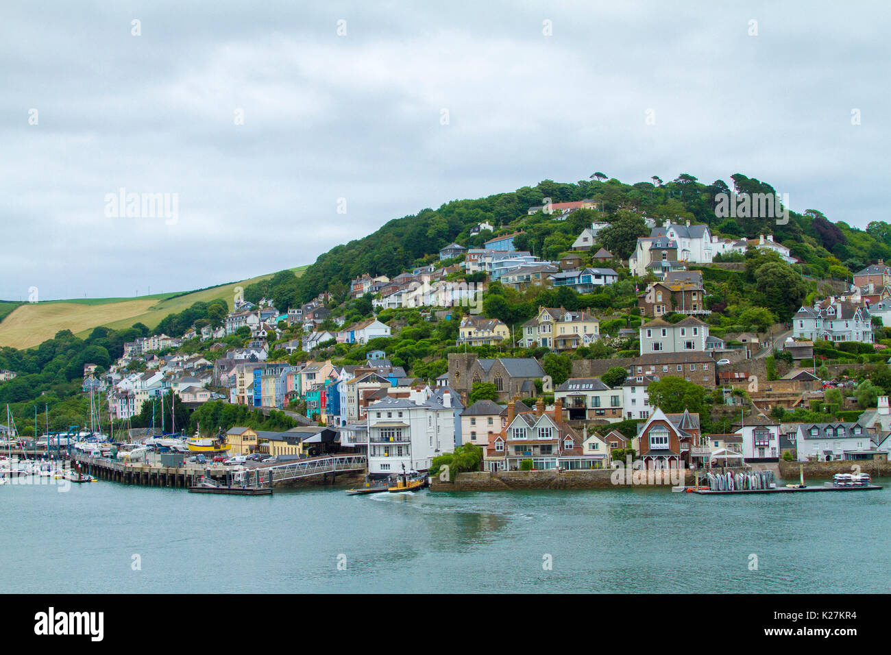 Coastal town of Dartmouth with houses crammed on tree-cloaked hillside rising above harbour dotted with boats in Devon, England Stock Photo