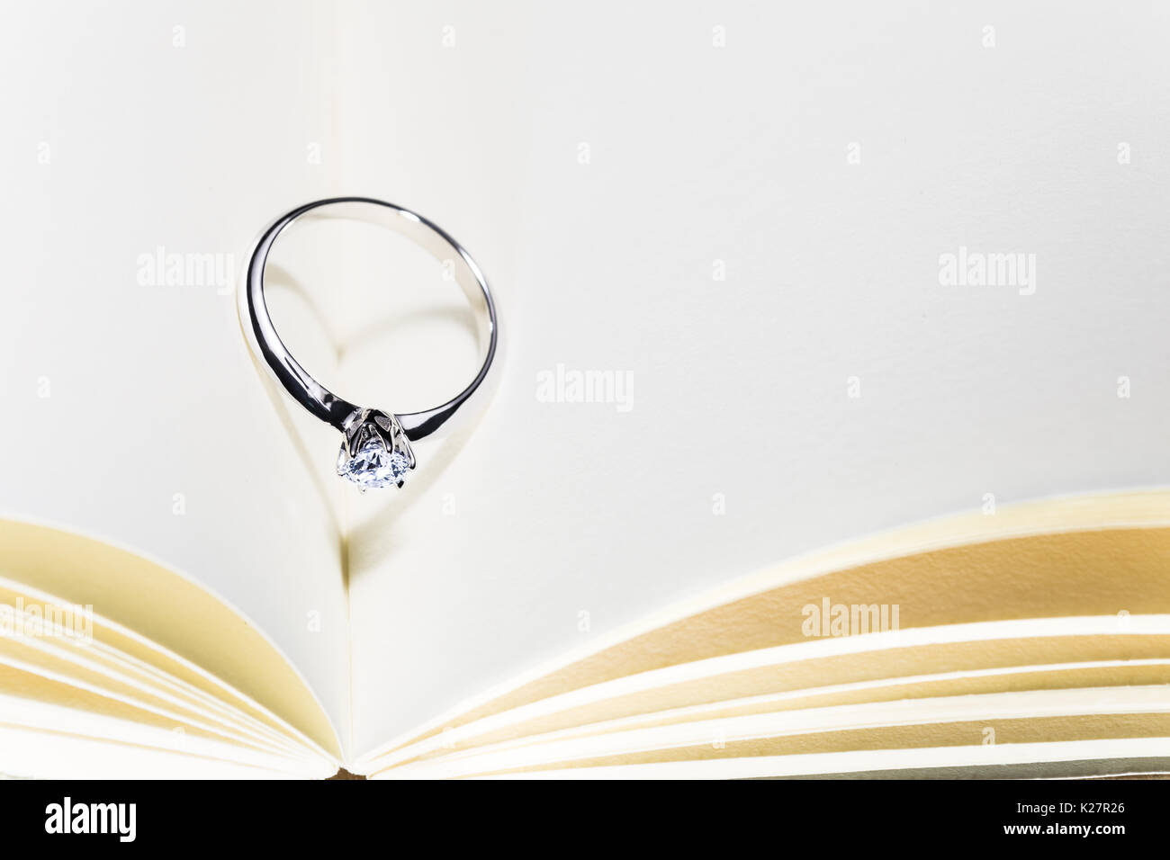 beautiful diamond ring on blank open book with heart shape shadow, room for copy space, good concept for wedding, engagement, or special occasions Stock Photo