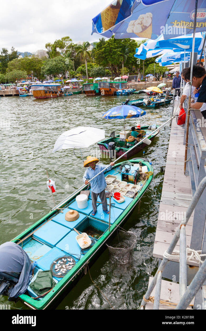 HONG KONG - JULY 13, 2017: Fishermen in boats alongside the Sai Kung harbor sell their live seafood catch to the public on the pier with the aid of a  Stock Photo