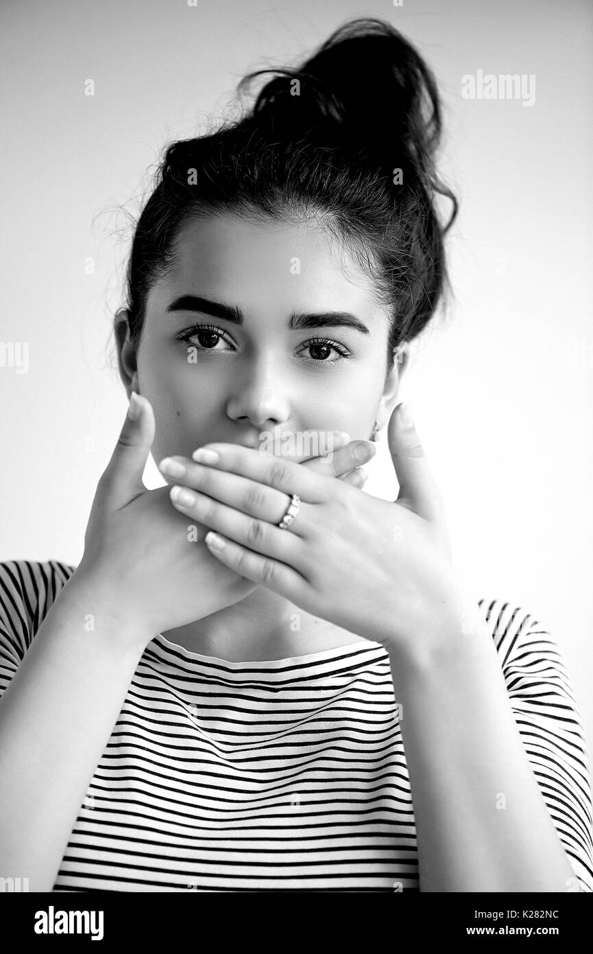Emotions. Close-up facial portrait.Speak no evil. Girl on a light background closes his mouth, , black and white Stock Photo