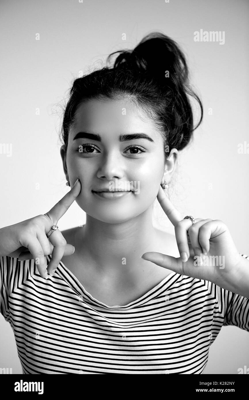 Surprised woman with hands up amazed or shocked by unexpected news holding close palms up and showing happy expression.Young adult woman on greybackground, black and white Stock Photo