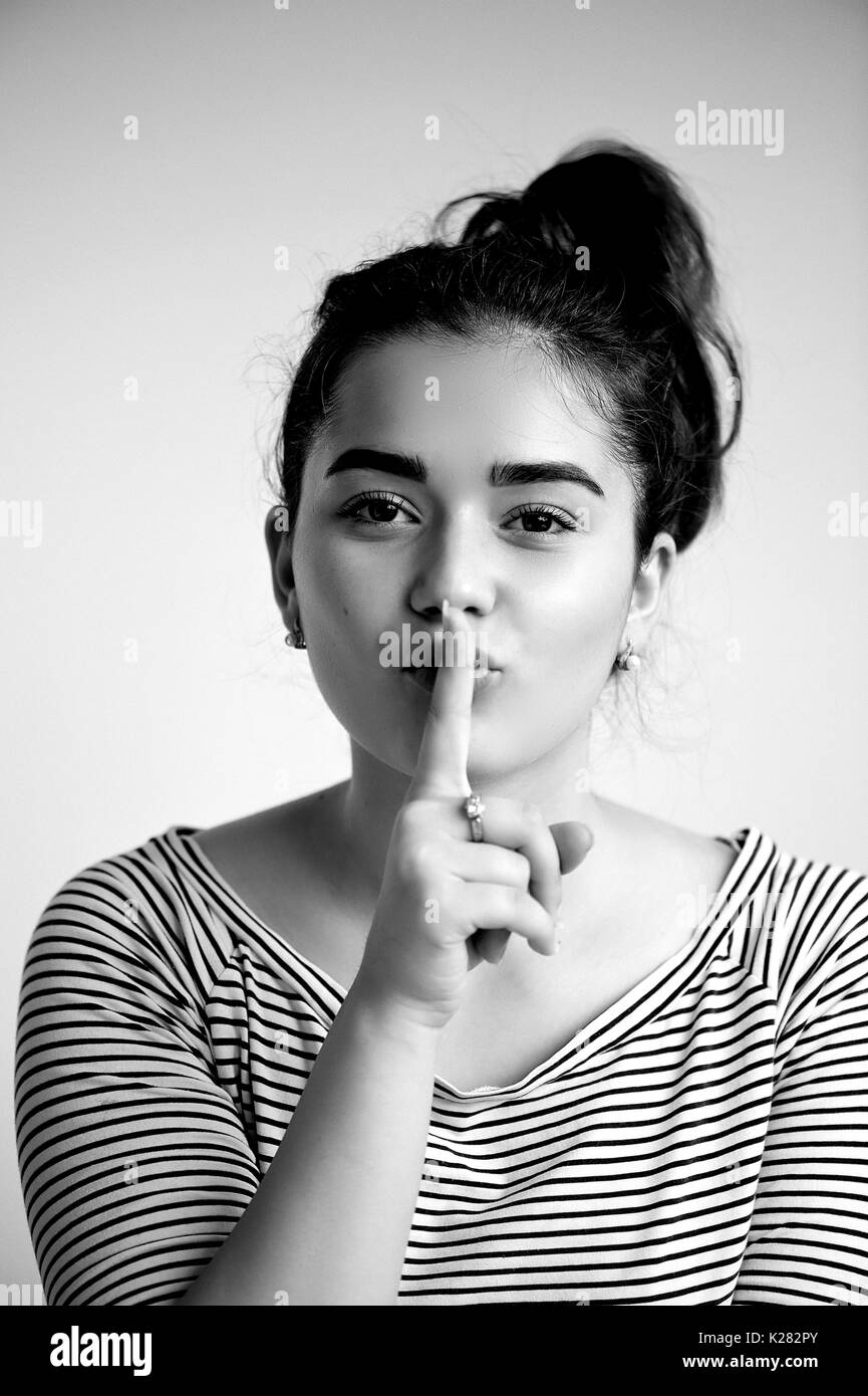 Beautiful young girl with dark hair and brown eyes. With clean glowing skin .Emotions. a finger to her lips, black and white Stock Photo