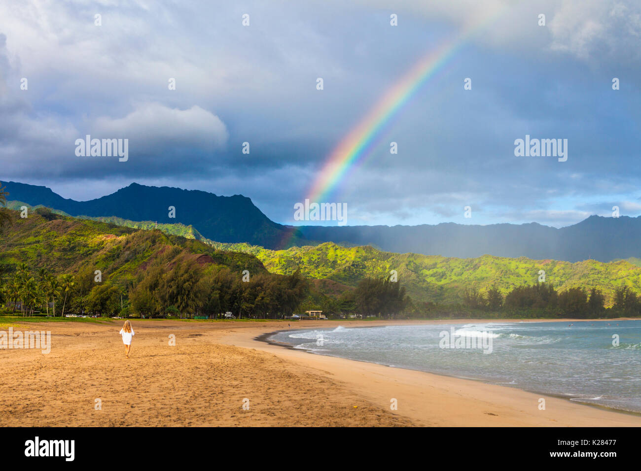 Woman walks at Hanalei Beach toward rainbow Stock Photo