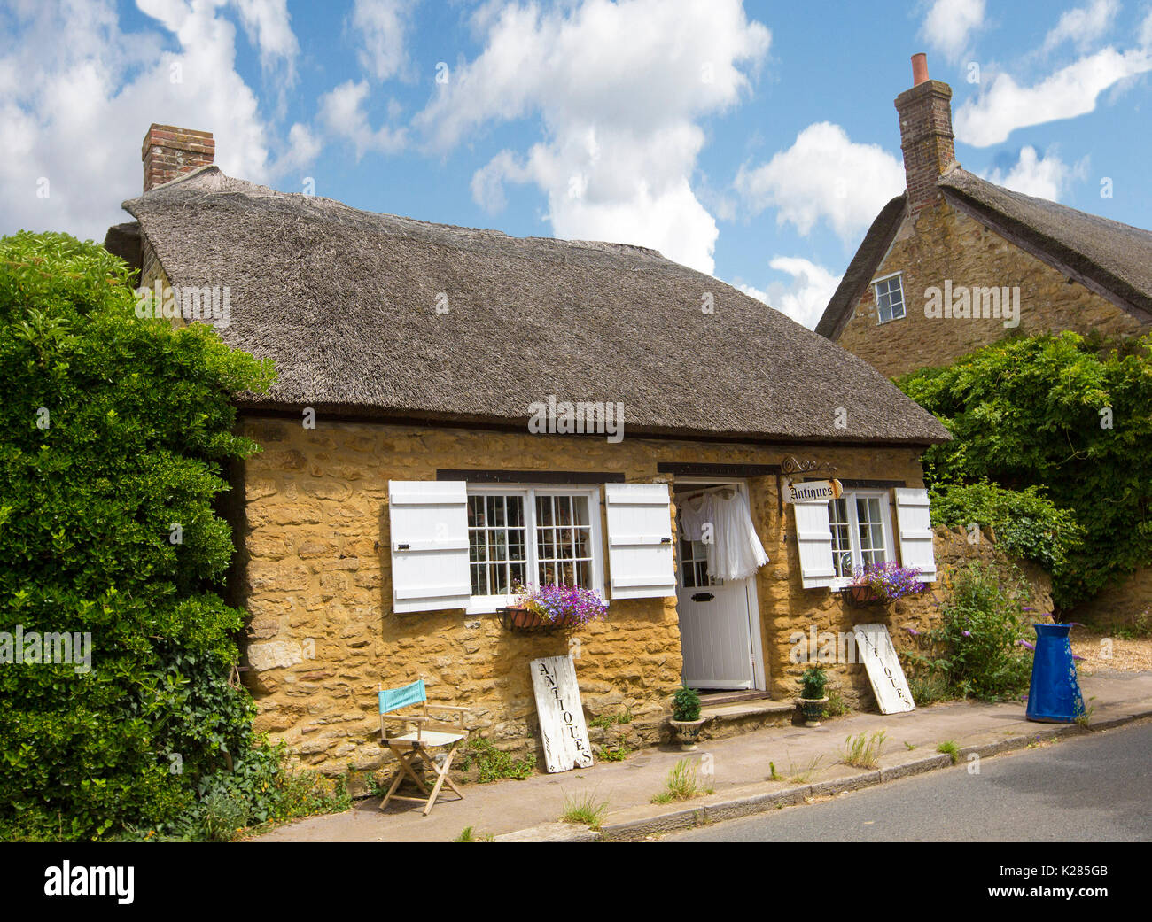 Stone cottage with thatched roof and window shutters, used as antique shop, at historic village of Abbotsbury, Dorset, England under blue sky Stock Photo
