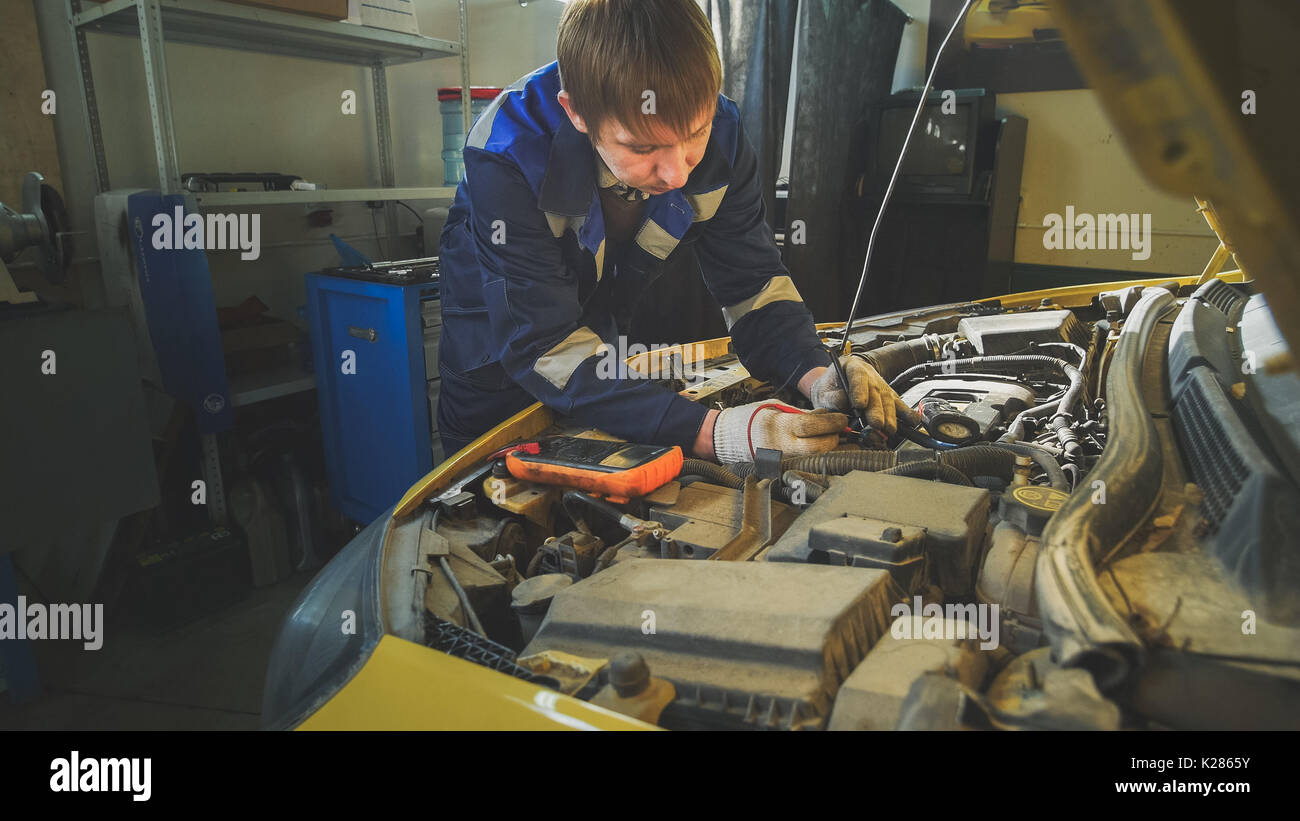 A mechanic checks the electrical in the hood of the car repairing in