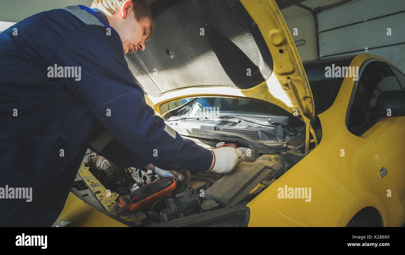 Mechanic in car repairing service diagnostics in engine compartment