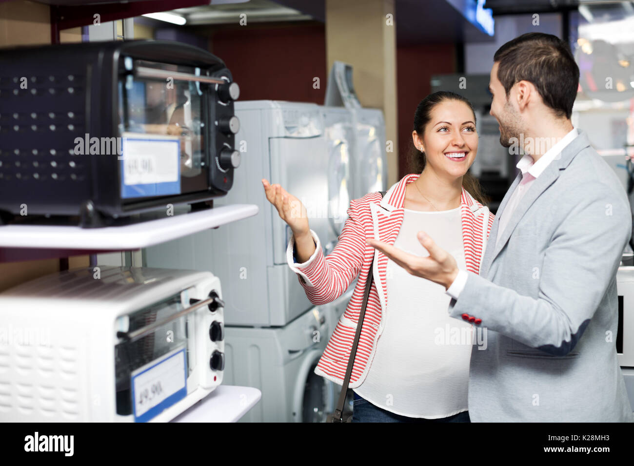 Smiling family couple choosing new microwave in supermarket. Focus on the woman Stock Photo